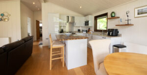 Bright open-plan kitchen with grey cabinets, island, and two wooden stools; warm wood floor and adjacent round dining table.